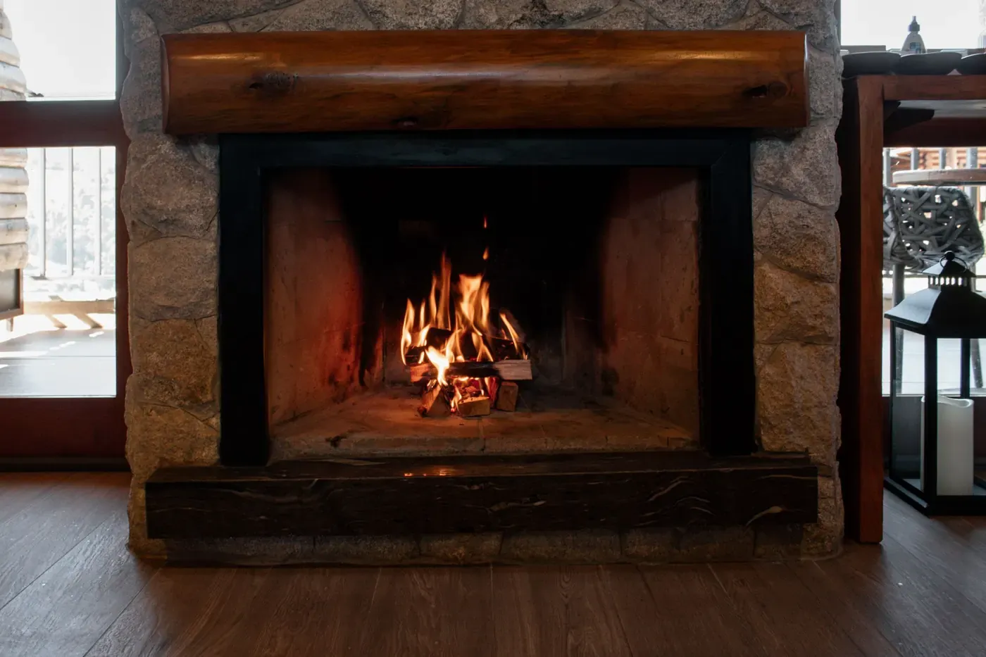 Stock photo of a wood fire burning in a stone fireplace with a black metal surround, a polished log mantel and a dark wood hearth