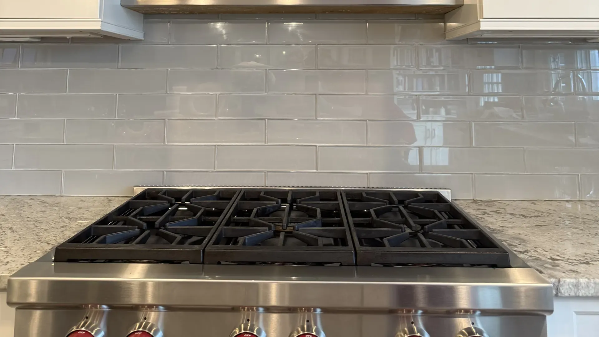 Wolf gas rangetop with red knobs under a stainless Vent-A-Hood after a steam cleaning, glass subway tile backsplash