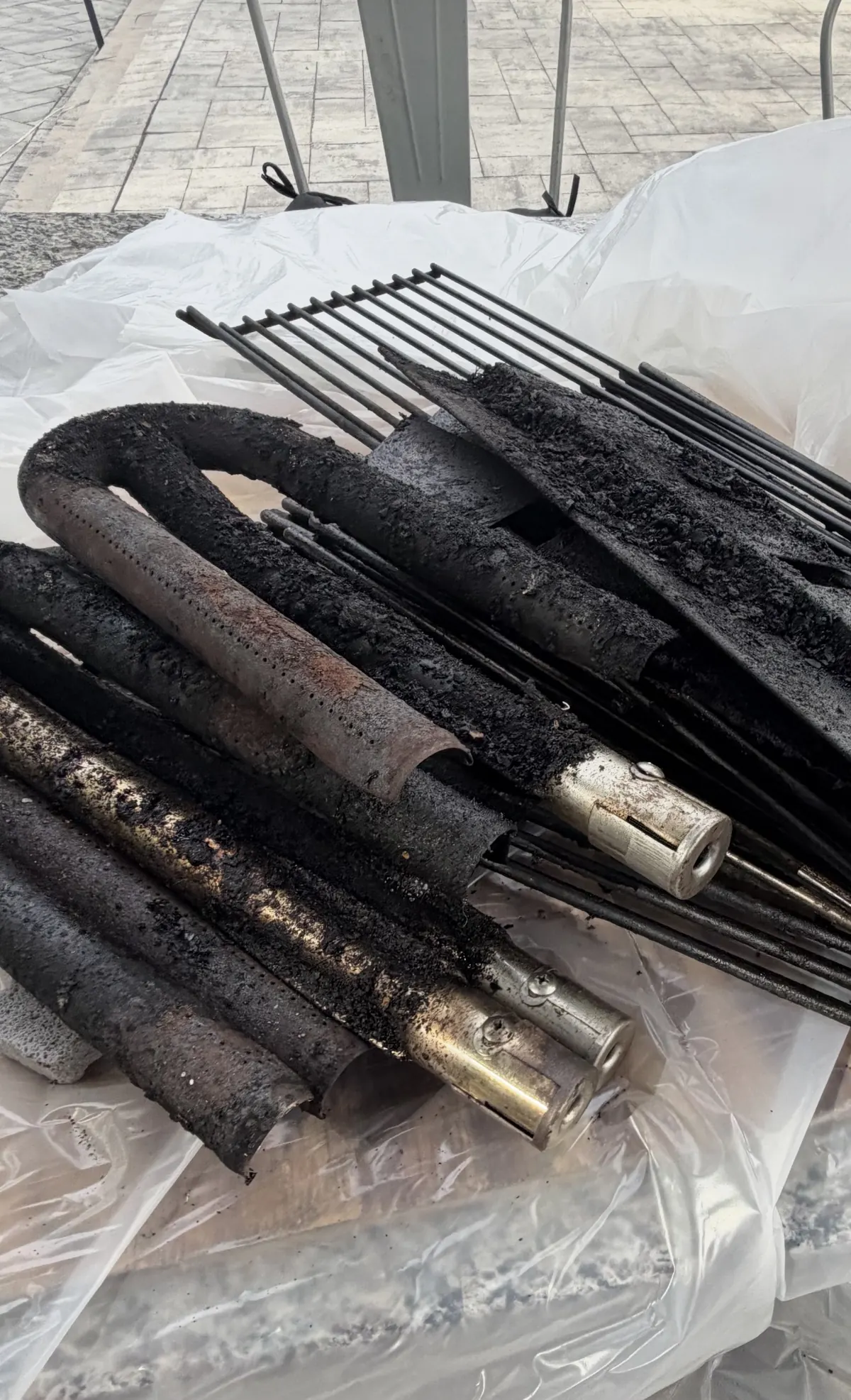 Built-in gas grill burner tubes removed and laid on a drop cloth, heavily caked with black carbon and grease before cleaning