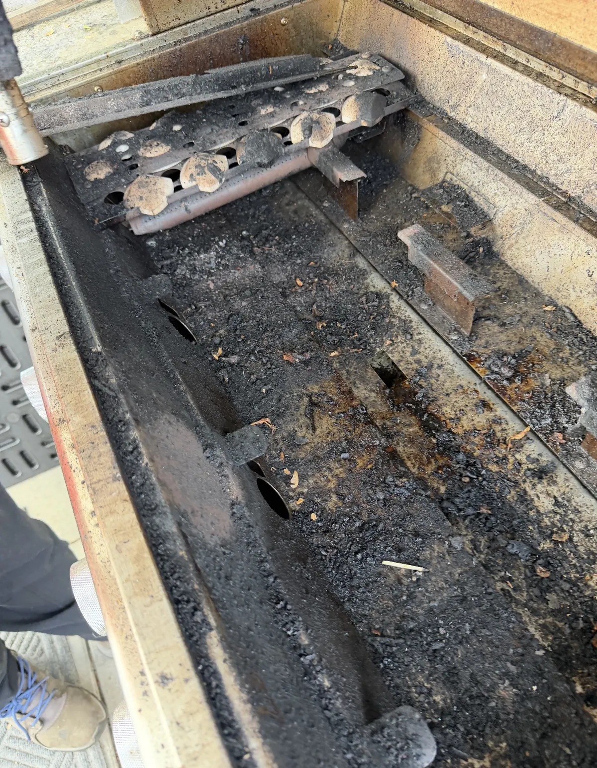 Lower housing of a built-in outdoor grill full of grease, ash and food debris before cleaning